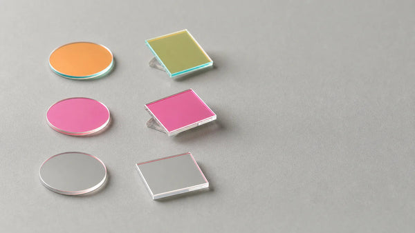 Several threaded machine vision bandpass filters showing dichroic coating reflections beside an M12 lens
