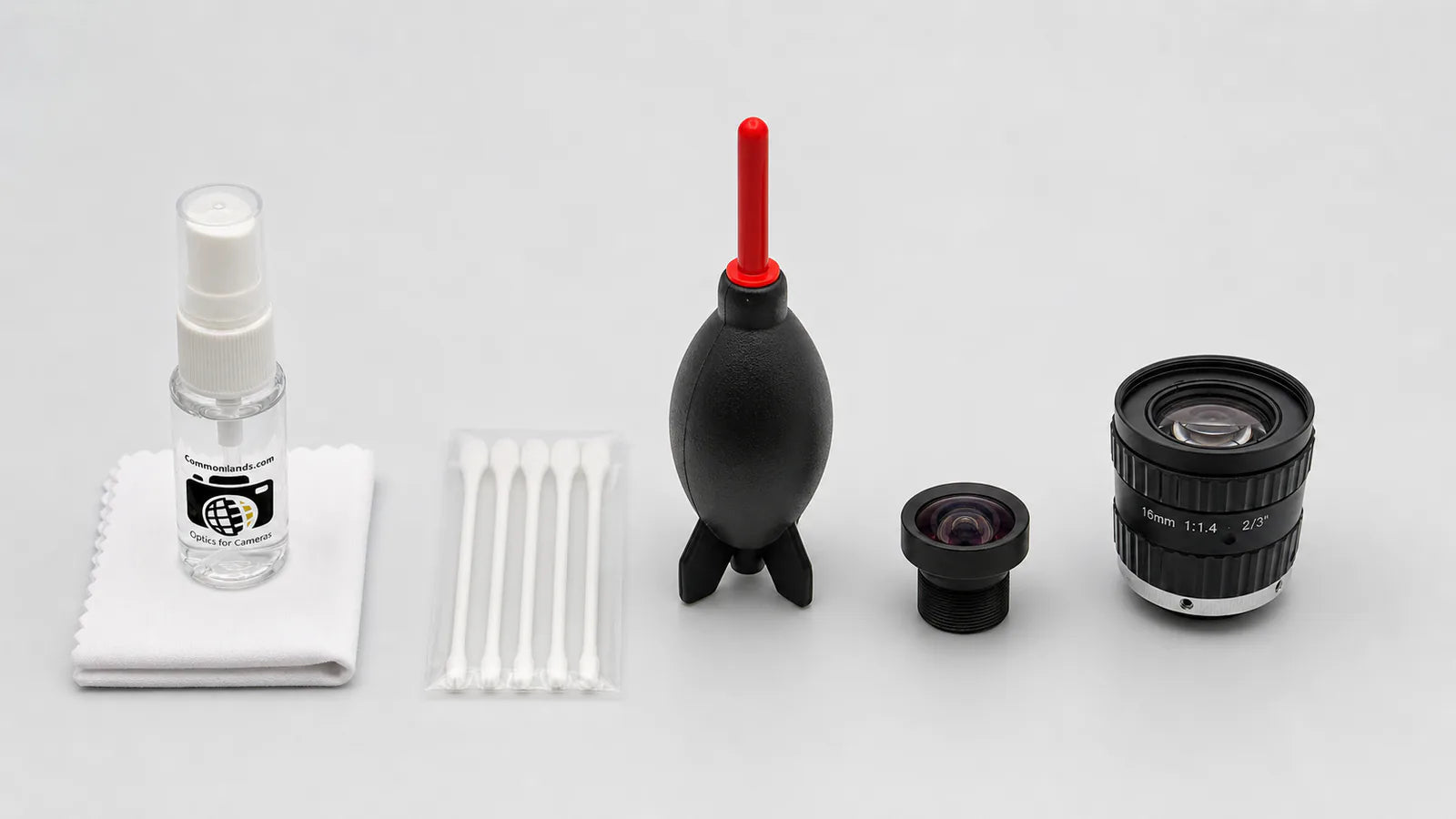 A lens cleaning kit with blower, brush, swabs, and solvent around two lenses