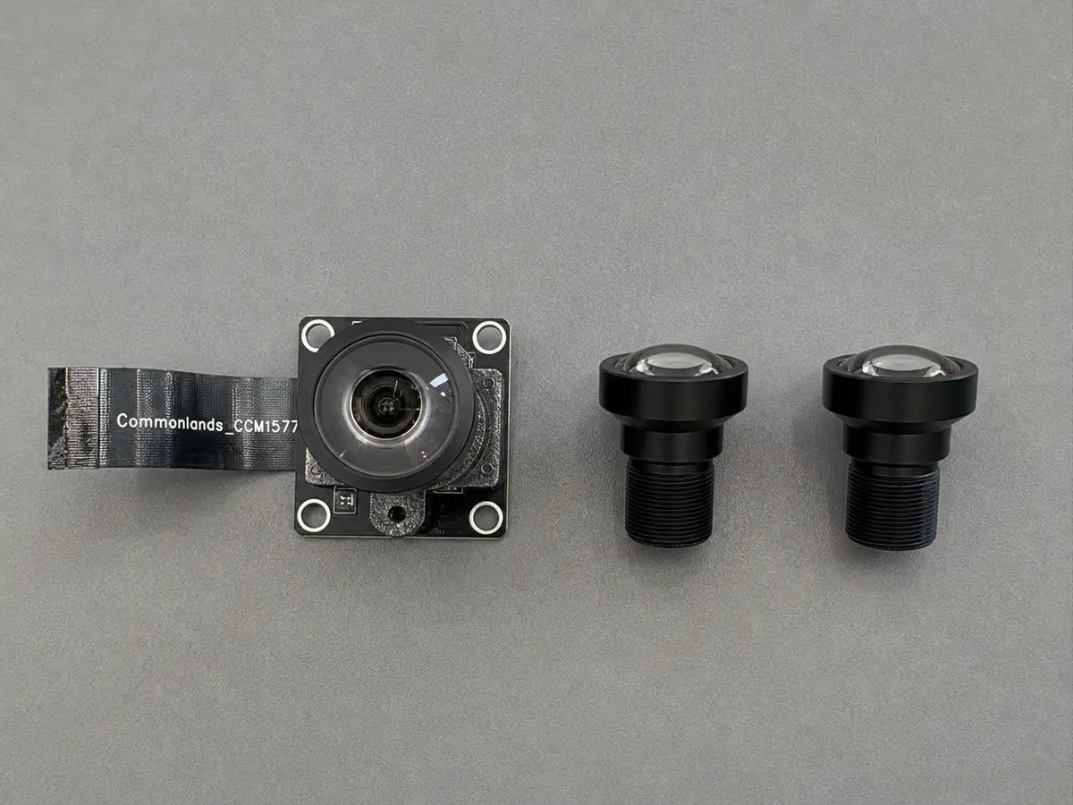Tweezers hold a small lens element at an angle above a bare image sensor