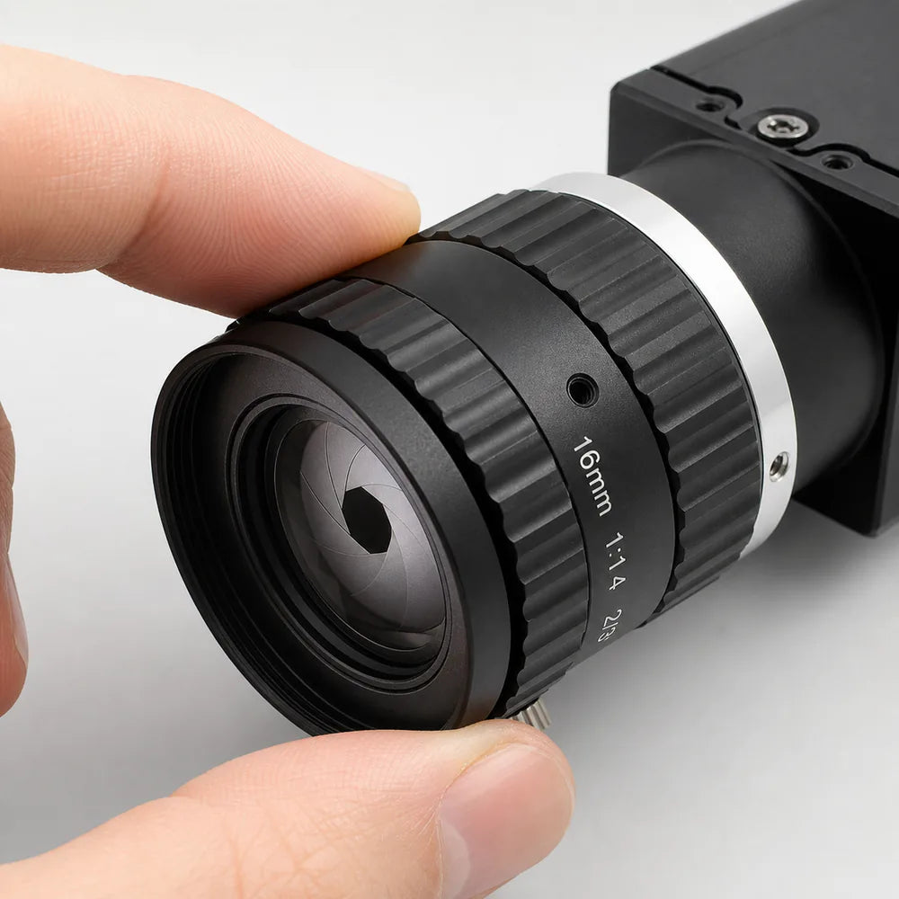 A hand turning the knurled iris ring on a Commonlands C-mount lens to move the aperture blades